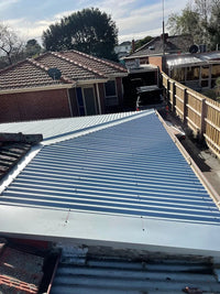 Metal roof with striped pattern, surrounded by residential buildings and trees.