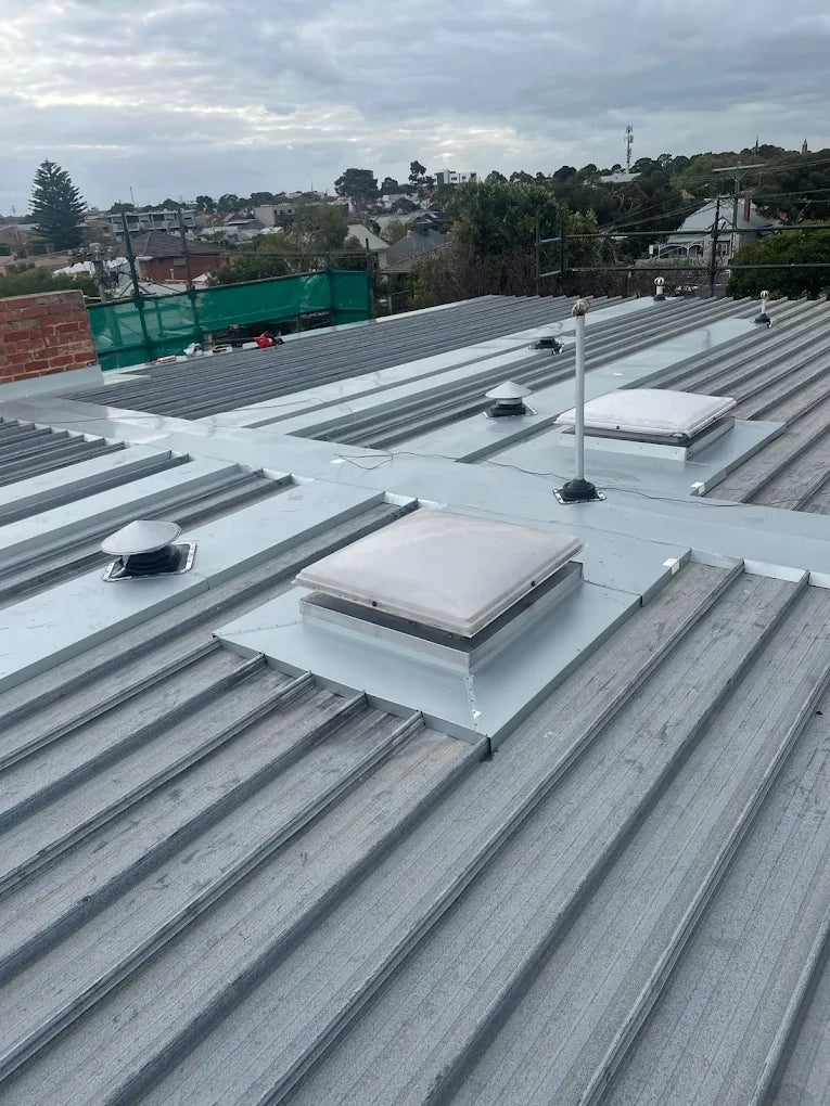 Roof with multiple roof lights and ventilation systems under a cloudy sky.