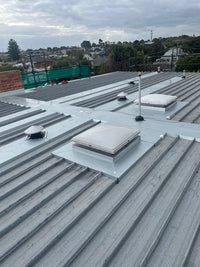 Roof with multiple roof lights and ventilation systems under a cloudy sky.