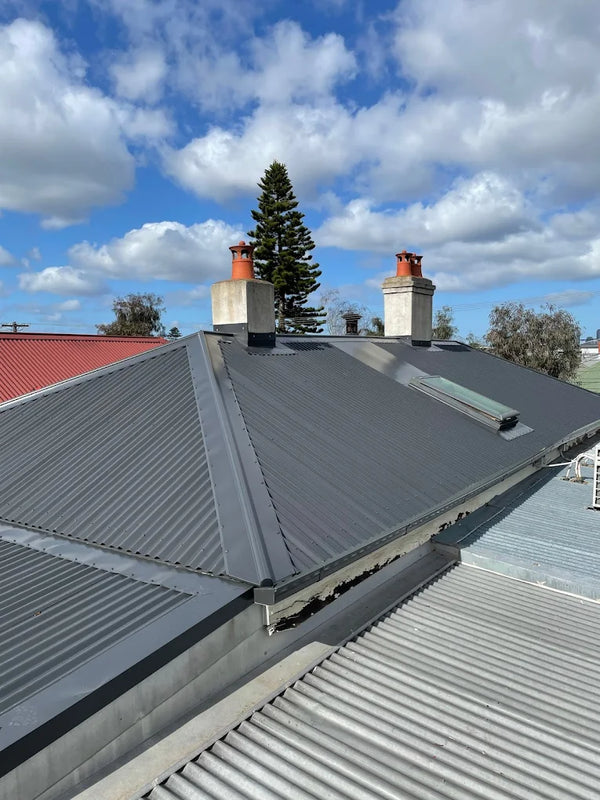 Roof with metal shingles and chimneys against a blue sky with clouds - Bill Roofing 