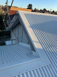 Metal roof with a gable end and solar panels on a clear day.