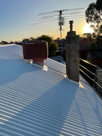 White roof with a red air conditioning unit and antenna against a sunset sky.
