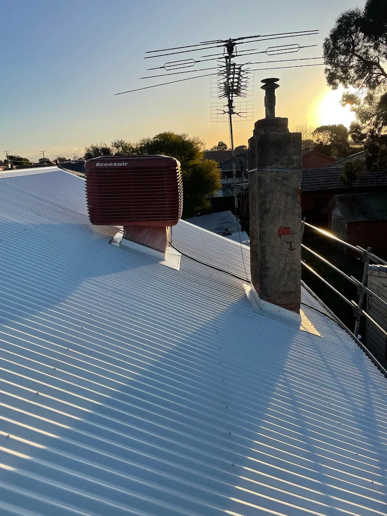 White roof with a red air conditioning unit and antenna against a sunset sky.