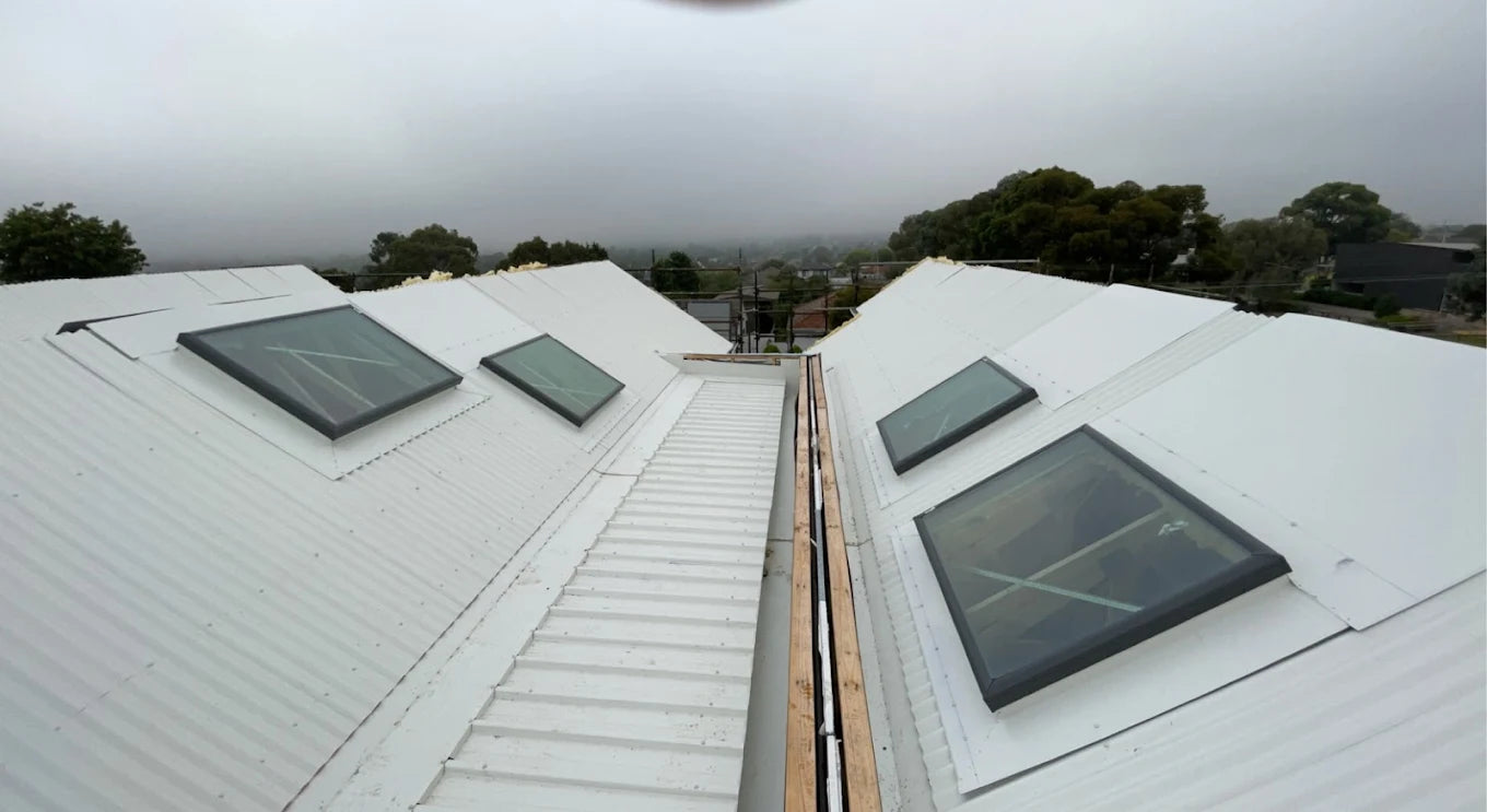 Two white rooftops with skylights on a cloudy day. - Bill Roofing 
