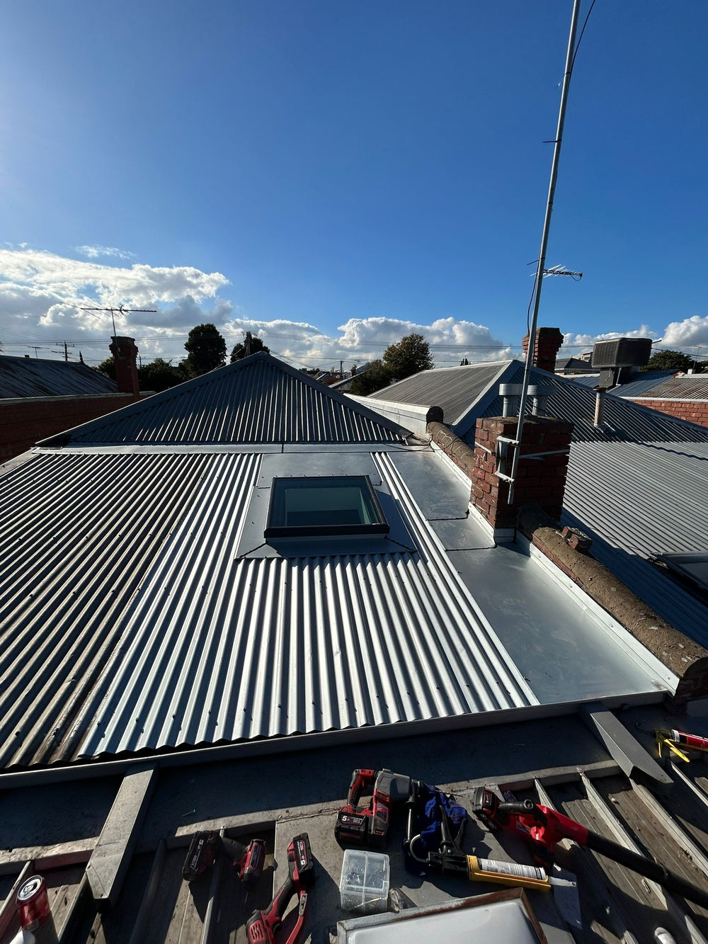 Roof with metal shingles and a skylight, under a clear blue sky. - Bill Roofing 
