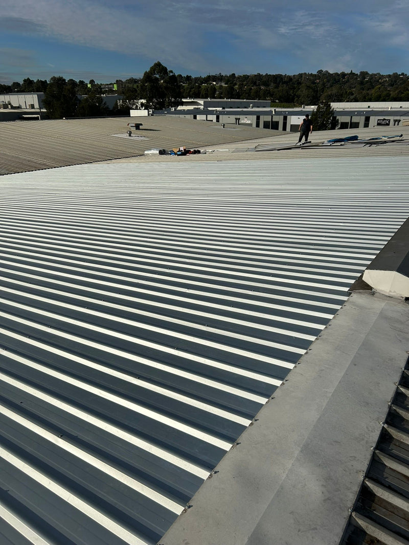 Roof with corrugated metal panels under a clear blue sky - Bill Roofing 