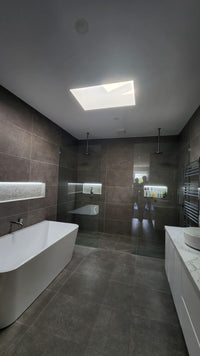 Modern bathroom with dark tiled walls, a white freestanding bathtub, and a skylight. - Bill Roofing 