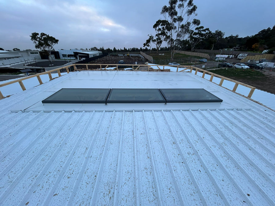 Roof with skylights and surrounding area with trees and buildings - Bill Roofing 