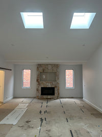 Living room with stone fireplace and skylights, under construction. - Bill Roofing 