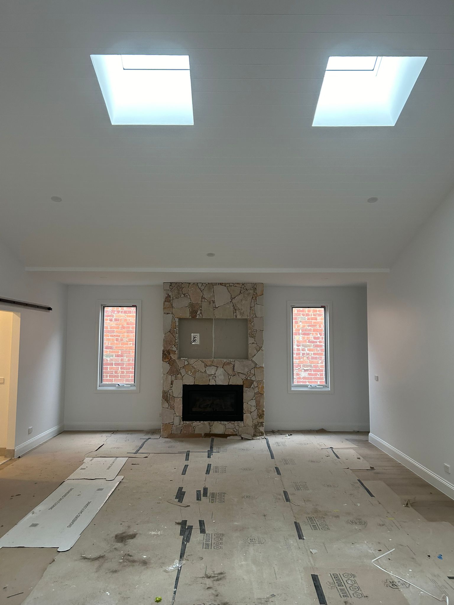 Living room with stone fireplace and skylights, under construction. - Bill Roofing 