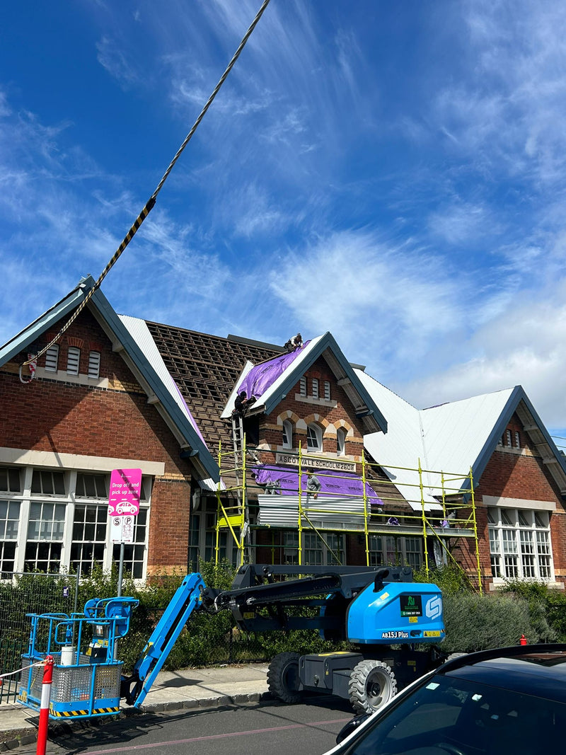 Building under renovation with scaffolding and a blue crane against a blue sky. - Bill Roofing 