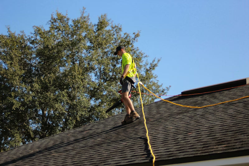 Person on a roof with a ladder and tools, against a clear blue sky.